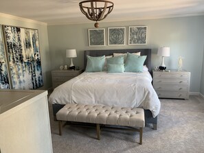 Cozy retreat with a large bed, tufted headboard, and plush pillows, accompanied by a bench, nightstand, and dresser.