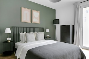 Een moderne slaapkamer met een bed, twee nachtkastjes met lampen, een kledingkast en twee abstracte schilderijen aan de muur.