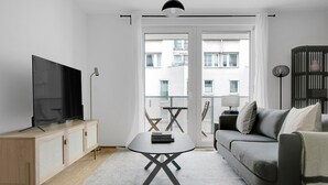 Een moderne woonkamer met een flatscreen televisie, een houten kast, een grijze bank en een kleine tafel.