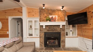 A cozy living room with a stone fireplace, a flat-screen TV mounted on the wall, a beige sofa, and a wooden coffee table.