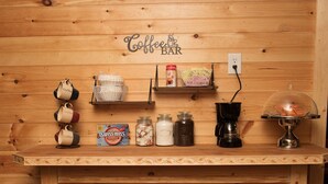 A wooden bar counter with a coffee station, including mugs, a coffee machine, and jars of condiments.