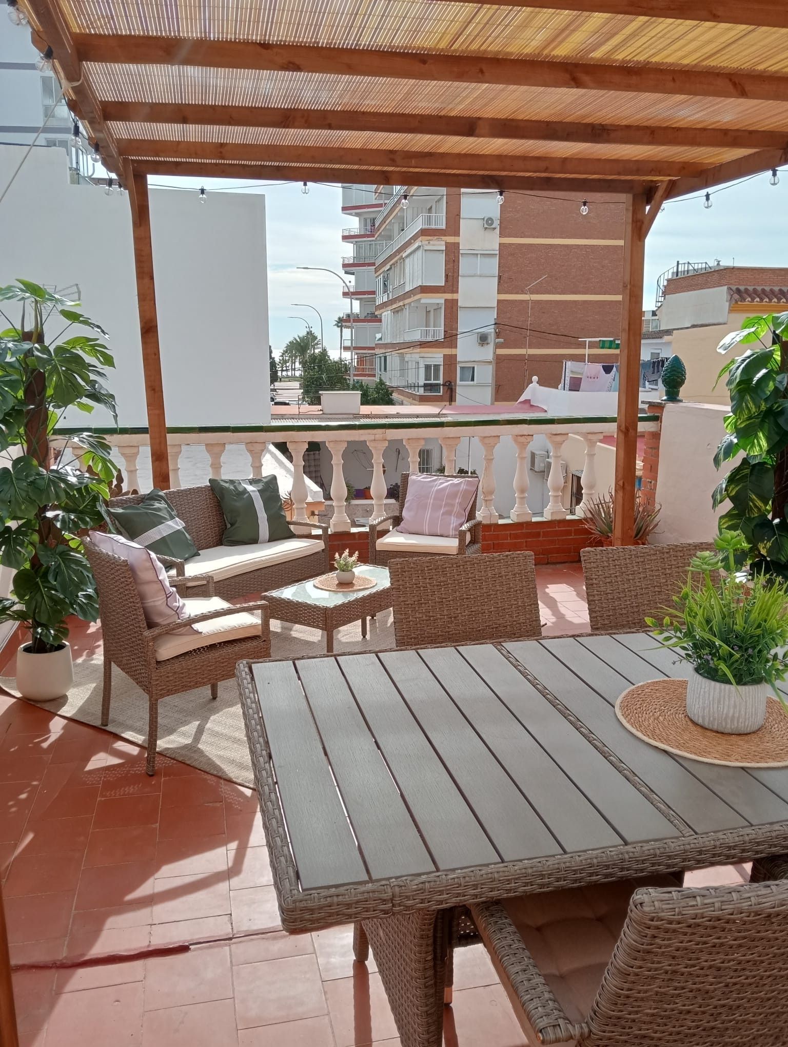 Un espacio de estar al aire libre cubierto, con mobiliario de mimbre y plantas en macetas.