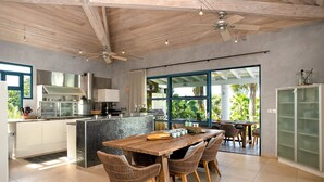 A modern kitchen with a large island, dining area with wicker chairs, and a view of the outdoors. - Les Palmiers Bleus | Ocean Front - Located in  Tropical Terres Basses with Private Pool (Saint Martin)