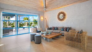 A spacious living area with a large window, a round mirror, and a wooden ceiling. - Les Palmiers Bleus | Ocean Front - Located in  Tropical Terres Basses with Private Pool (Saint Martin)