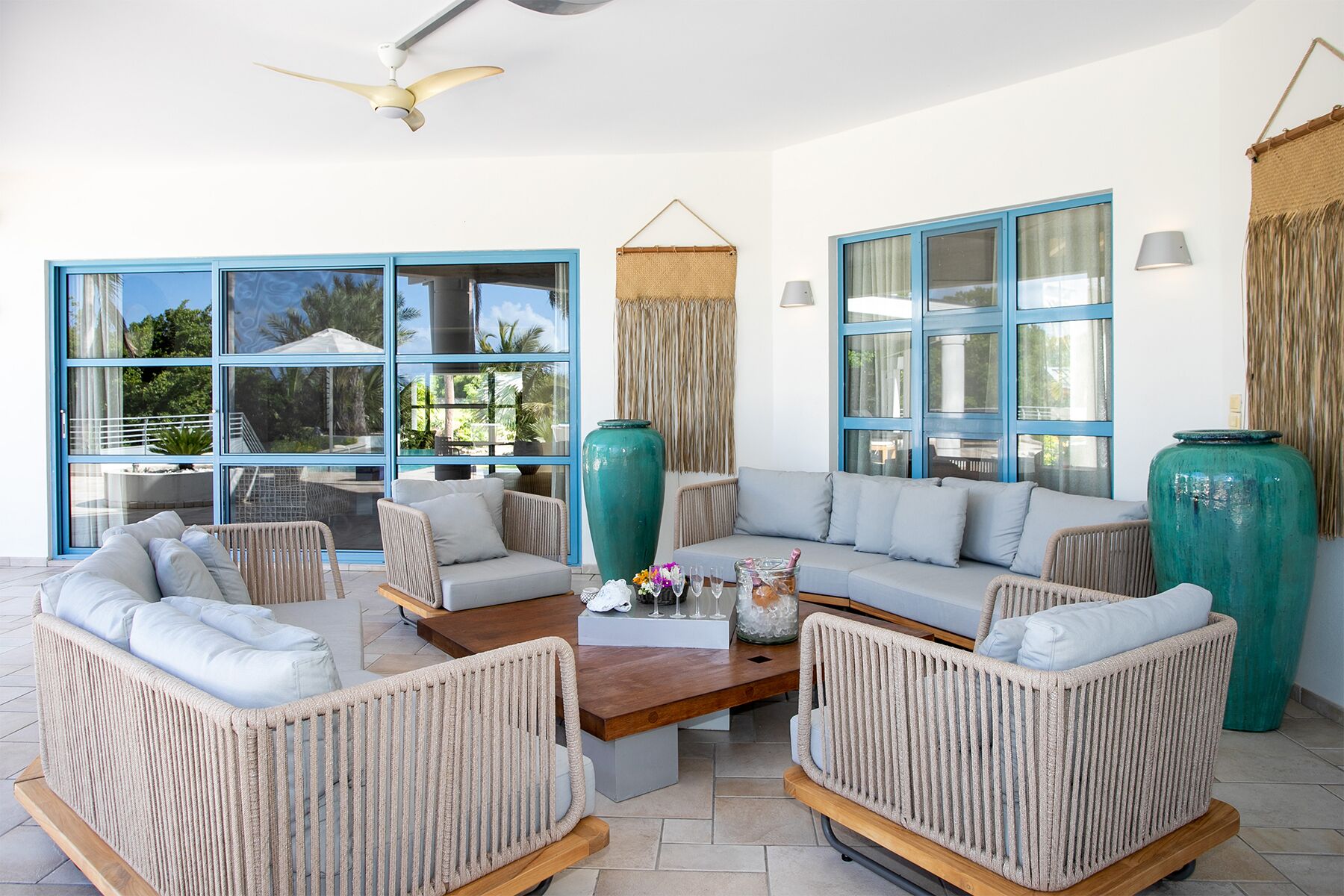 A spacious living room with a sectional sofa, two armchairs, a coffee table, and large windows with blue frames.