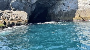 A rocky coastline with a cave entrance and clear blue water. - Guest house da torre (Sao Pedro da Aldeia)