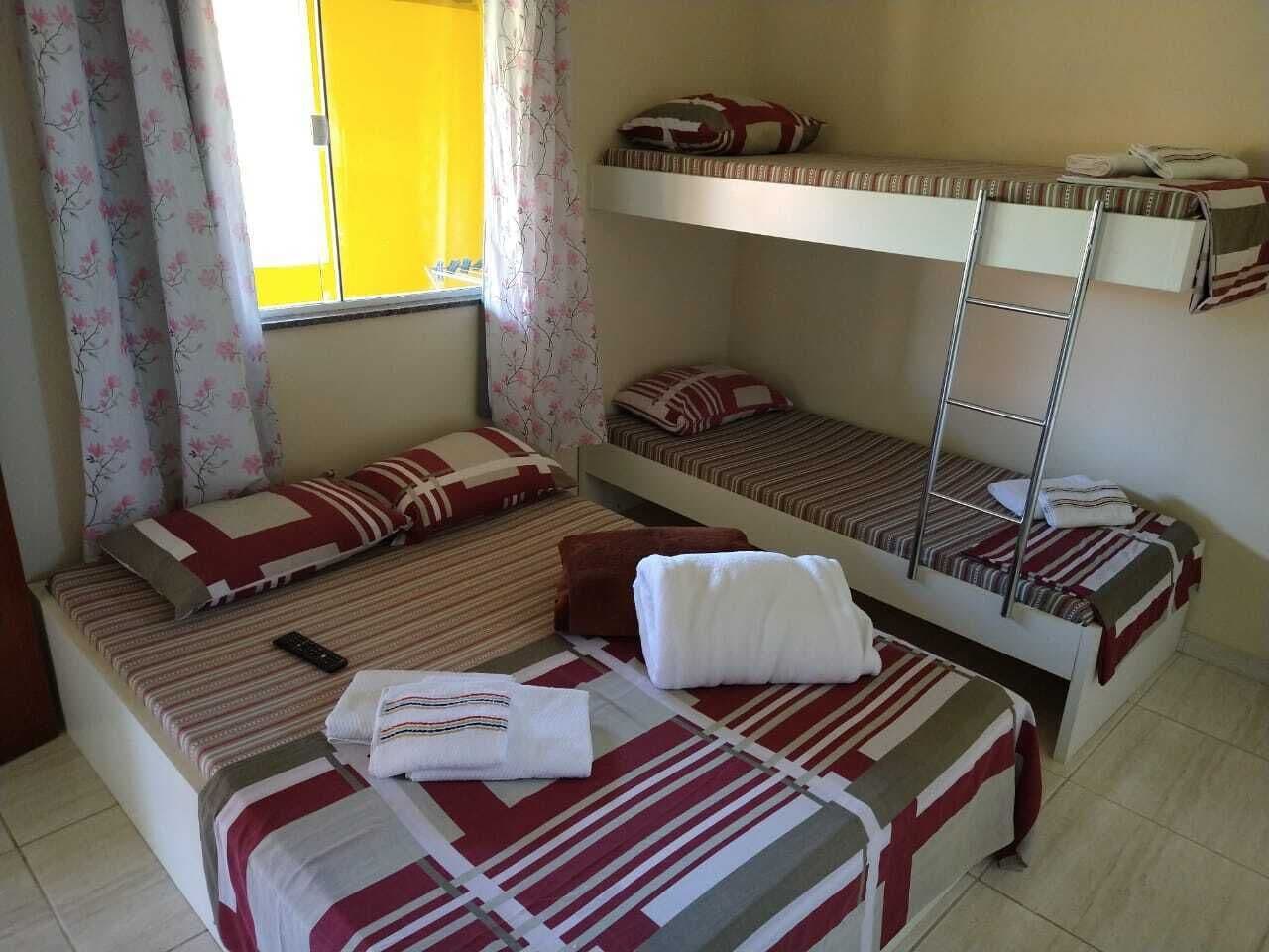 Un dormitorio con literas, una ventana con cortinas amarillas y un control remoto sobre la cama.