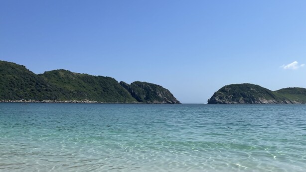 A beach with clear shallow waters and distant green hills. - Guest house da torre (Sao Pedro da Aldeia)
