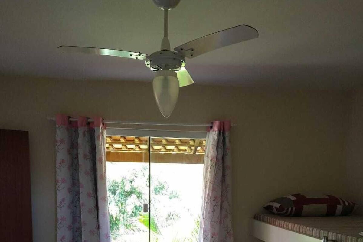 A dormitory room with bunk beds, a ceiling fan, a window with curtains, and a bed with a striped blanket and pillows.