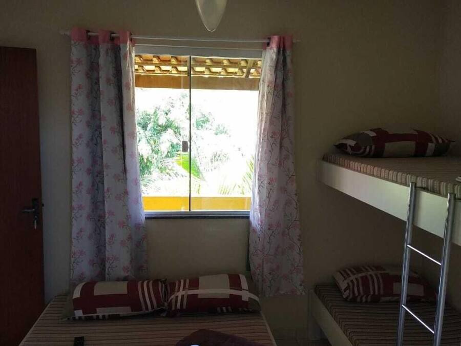 Ein Schlafsaalzimmer mit Etagenbetten, einem Deckenventilator, einem Fenster mit Vorhängen sowie einem Bett mit einer gestreiften Decke und Kissen.
