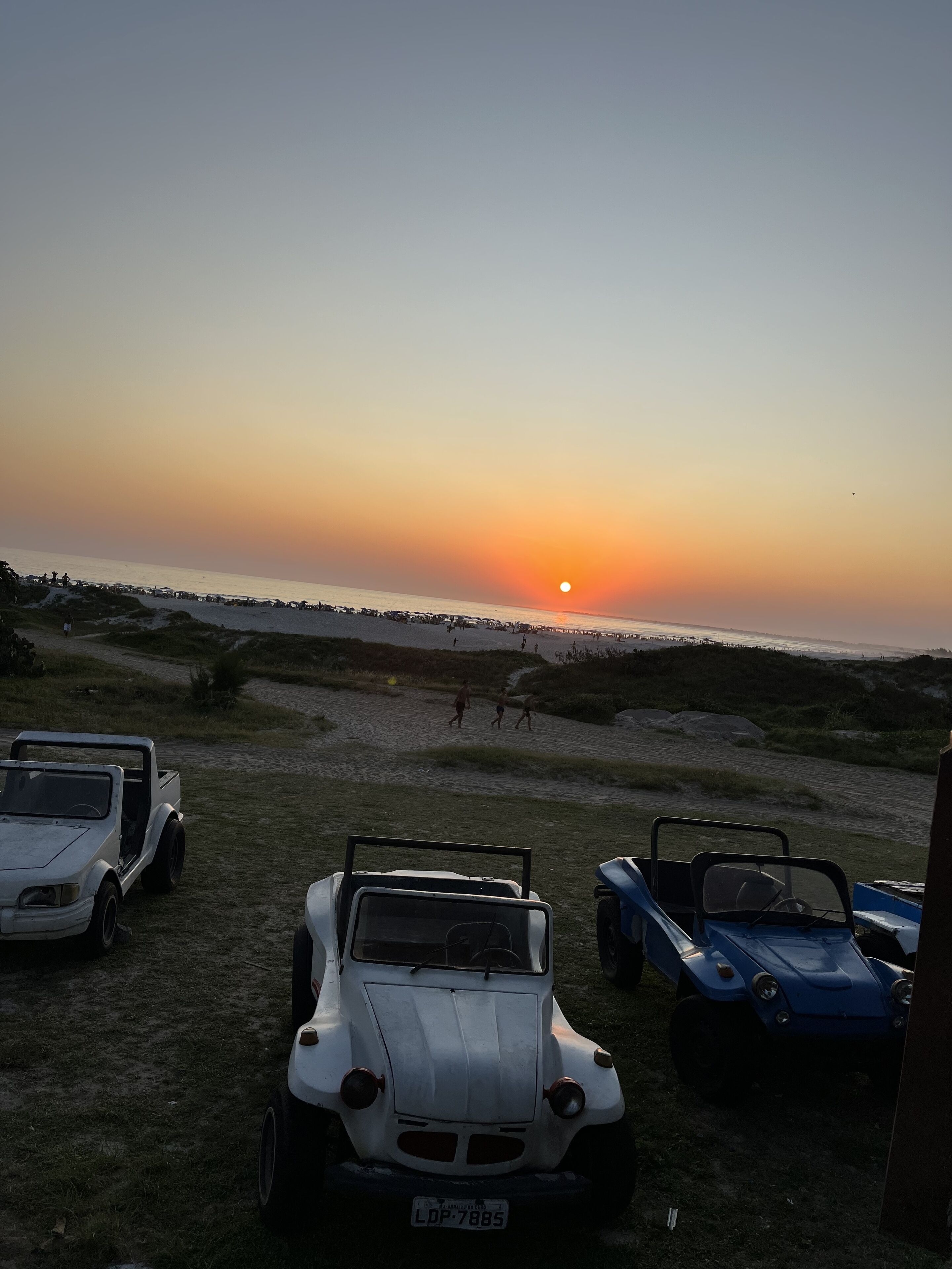 Un coucher de soleil sur une plage, avec des véhicules garés et un ciel dégagé.