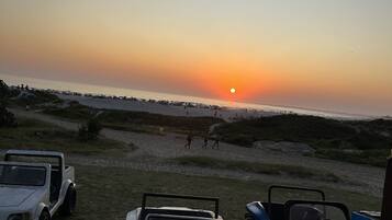 Un coucher de soleil sur une plage, avec des véhicules garés et un ciel dégagé.