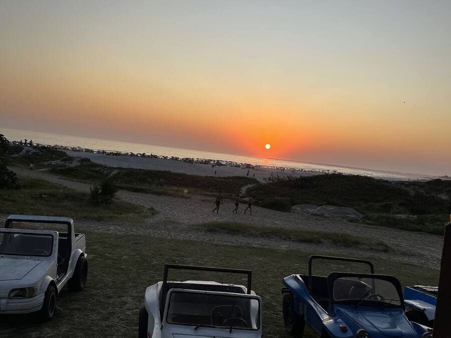 Un coucher de soleil sur une plage, avec des véhicules garés et un ciel dégagé.