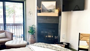 Un dormitorio con cama, chimenea, televisor y balcón con vistas.