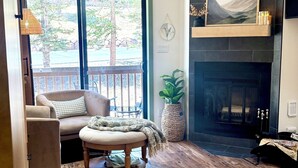 Una sala de estar con chimenea, un ventanal grande y piso de madera.