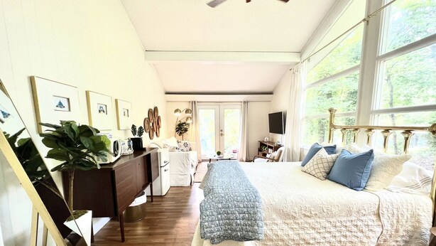 Ein geräumiges Schlafzimmer mit einem großen Bett, einem Schreibtisch und einem Stuhl. Ein Deckenventilator und ein Fenster sorgen für natürliches Licht.