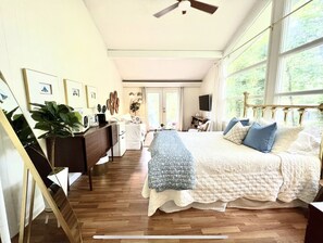 Une chambre spacieuse avec un grand lit, un bureau et une chaise. Elle est équipée d’un ventilateur de plafond et d’une fenêtre qui laisse entrer la lumière naturelle.