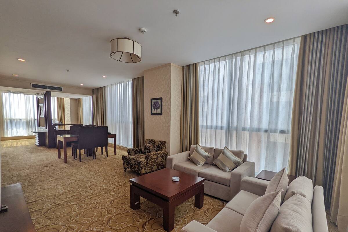 A hotel room with a living area featuring a sofa, armchairs, a coffee table, and a dining set.