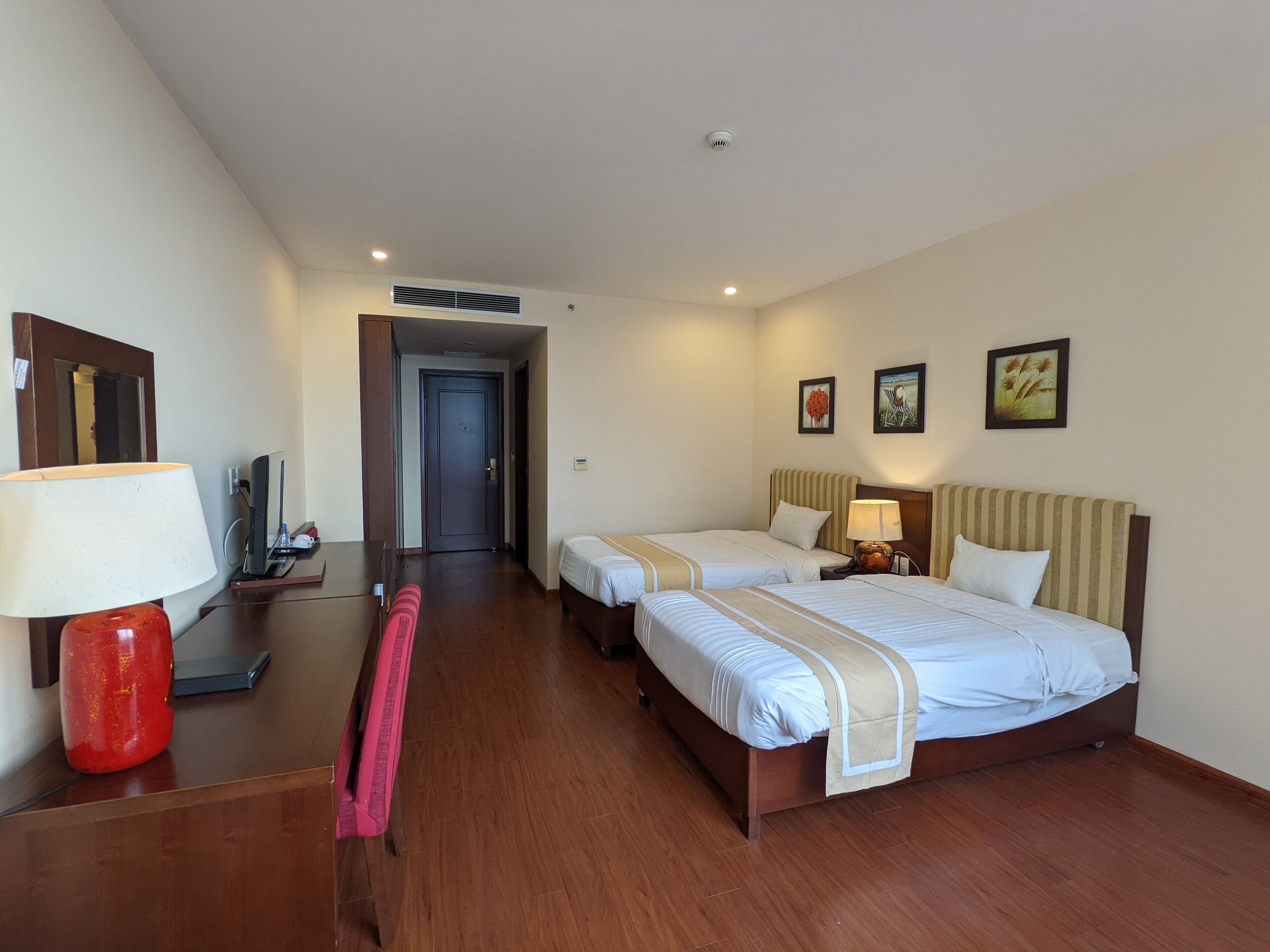 A hotel room with two beds, a desk with a lamp, a TV, and a red chair.