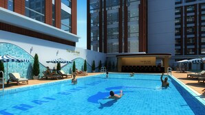 Una piscina con sillas de descanso y sombrillas, rodeada de edificios altos.