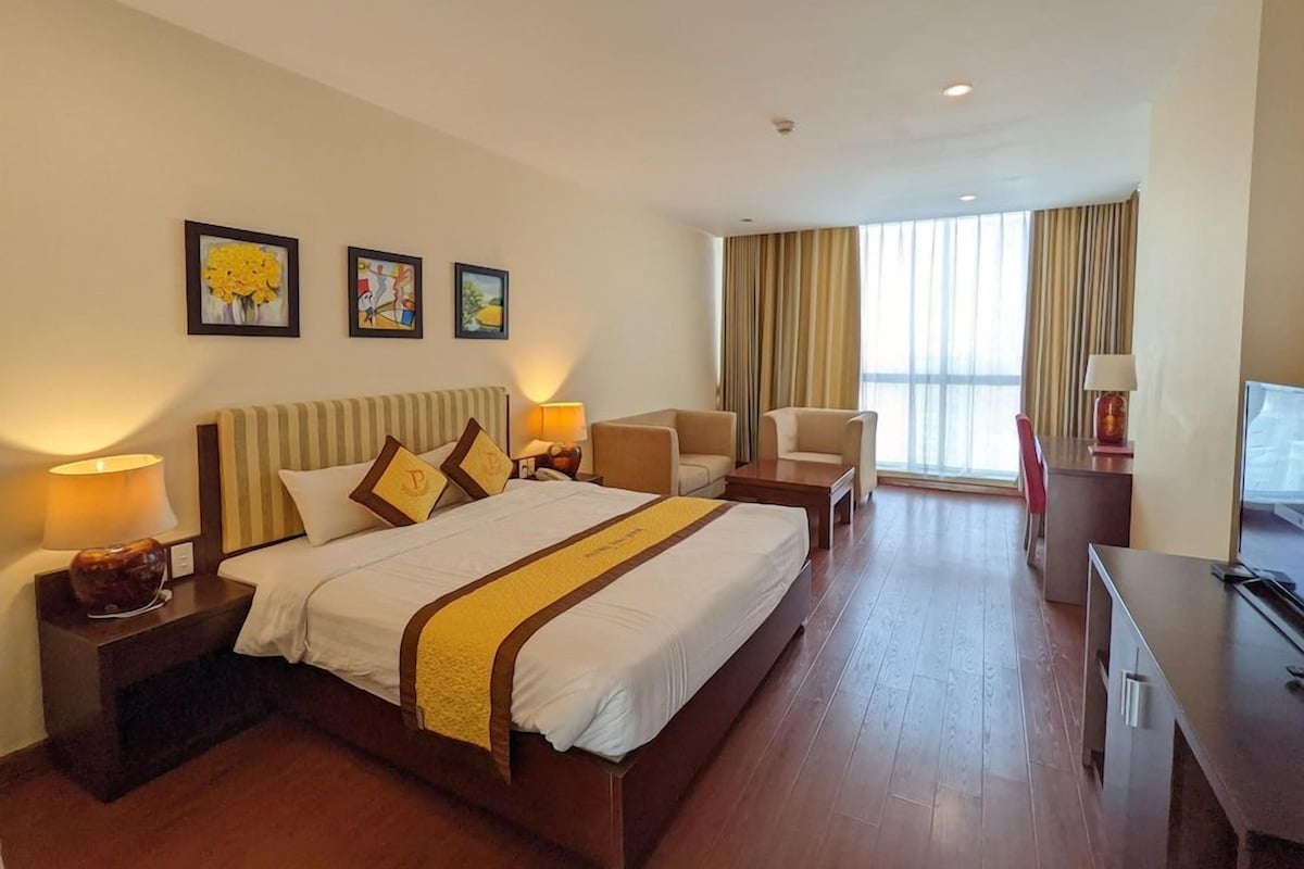 A hotel room with a large bed, bedside tables, a desk, and a chair. There are three framed pictures on the wall.