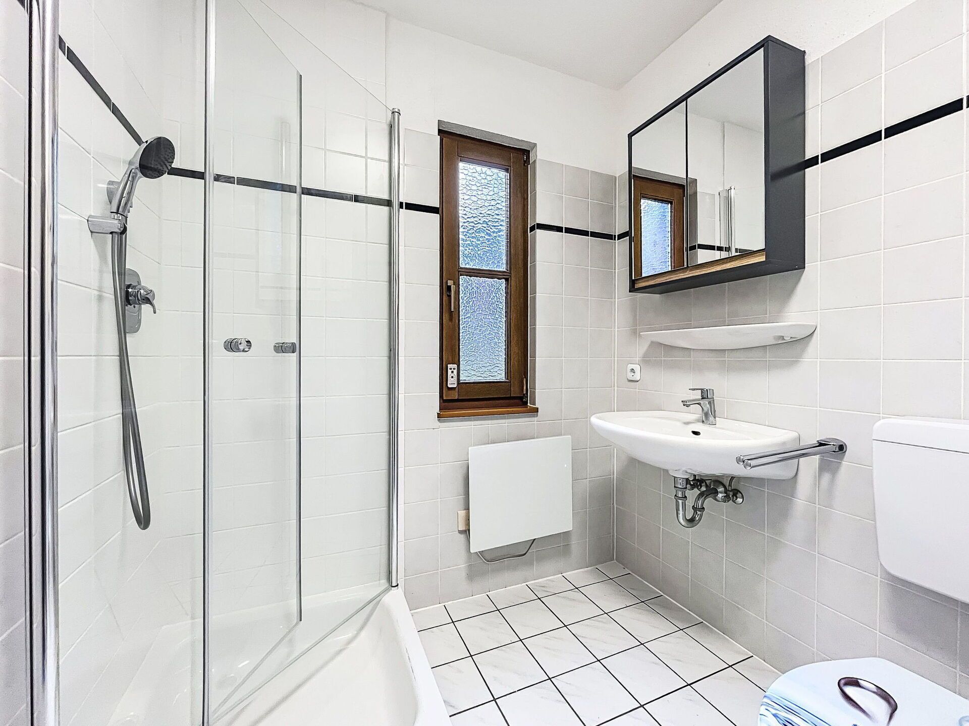 Un baño moderno con ducha de vidrio, lavamanos blanco y un inodoro.