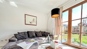 A modern living room with a grey sofa, a glass coffee table, and a large window with a view of greenery. - Cosy apartment in villa for 6 guests with WIFI, TV, terrace and pets allowed (Bad Wildungen)