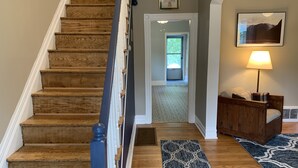A wooden staircase leading to a door, a patterned rug, a lamp, and a couch in a hallway.