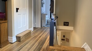 A hallway with wooden flooring, a white door, and a view into a bathroom with a toilet and sink.