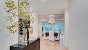 Un espace repas moderne avec une longue table, des chaises blanches et une grande fenêtre donnant sur l’extérieur.