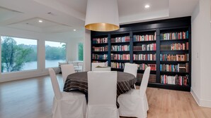 Une bibliothèque moderne dotée d’une grande étagère, d’une table ronde avec des chaises et offrant une vue sur un lac.