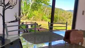 A modern room with a glass table, a decorative tree sculpture, and a view of a lush garden and mountains through large windows. - Mountain views and beautiful sunrises 🗻 (San Ramon)