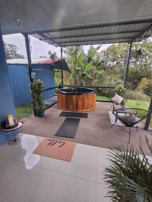 Um pátio externo com uma banheira de hidromassagem de madeira, uma cadeira, uma mesinha e um vaso de planta.