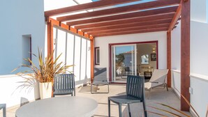 Un patio al aire libre con una mesa redonda y dos sillas, una pérgola de madera y una planta en maceta.