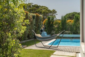 A hammock by a swimming pool with a view of lush greenery and trees. - LV Premier LA2 heated pool, AC, garden, sea view (Sesimbra)