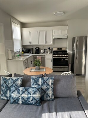 A modern kitchen with white cabinets, a stainless steel refrigerator, a gas stove, and a dining area with a round table and grey sofa. - 🗽15 Min to NYC! 🏙 Cozy 3 🛏 2 🛁 apartment! ♥️ 🛍🎶 (Union City)