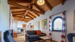 A cozy living room with wooden beams, a sofa, a coffee table, and a view of the outdoors through a window. - La Quercia by Interhome (Mondovì)