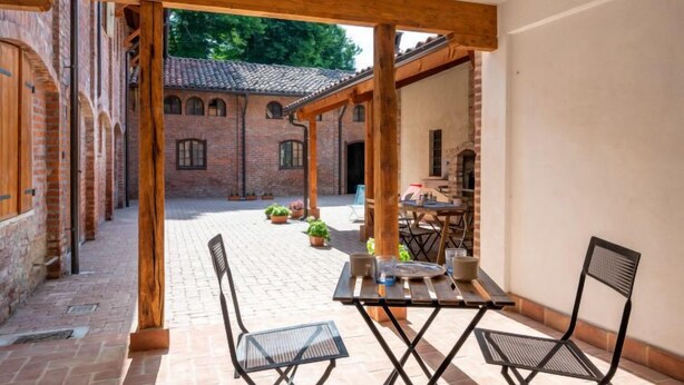 Área de pátio ao ar livre com piso de tijolos, pérgola de madeira e uma mesa posta para dois.