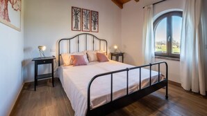 Quarto com cama, duas mesas de cabeceira, janela com cortinas e teto com vigas aparentes.