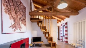 Uma sala de estar moderna com escada de madeira, uma pintura de uma árvore grande e um eletrodoméstico vermelho.