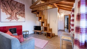 Uma sala de estar moderna com um sofá vermelho, uma poltrona azul, uma escada de madeira e uma pintura de uma árvore grande na parede.