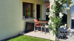 Une terrasse avec une table et des chaises, une petite fenêtre et un arrangement floral.