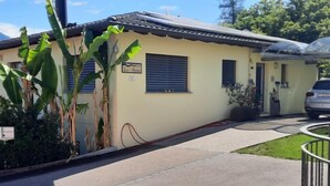 Une maison de plain-pied à la façade beige, avec une enseigne indiquant  « La Casa », et un petit jardin agrémenté de bananiers.