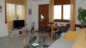 Un salon comprenant un téléviseur, un canapé, une table à manger, des chaises et une plante.