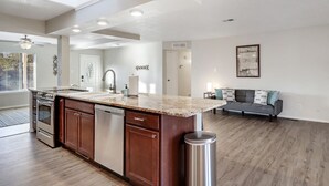 A spacious kitchen with a central island, built-in oven, and dishwasher. There is a dining area with a sofa and a painting on the wall. - Game Room - Mountain Views - King Bed - near Golf Course - Intel - Rust Medical  (Albuquerque)