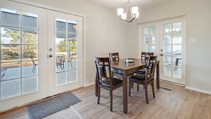A dining area with a wooden table and chairs, large windows, and a chandelier. - Game Room - Mountain Views - King Bed - near Golf Course - Intel - Rust Medical  (Albuquerque)