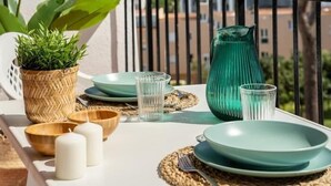 Un balcon avec une table dressée pour deux personnes, agrémenté d’un panier en osier, de bols en bois, de bougies et d’un vase vert.