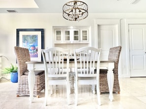 A dining area with a white table and chairs, a chandelier, and wicker chairs. - Upscale Beach Villa, 3-min to the beach, 6-seater Golf Cart, Steps to Pool (Miramar Beach)