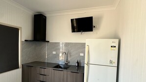 A compact kitchen with a built-in sink, a black range hood, a white refrigerator, and a flat-screen TV mounted on the wall. - Darwin Resort (Winnellie)