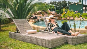 A person relaxing on wicker lounge chairs by a pool with a view of a rock formation and a small building in the background. - Darwin Resort (Winnellie)